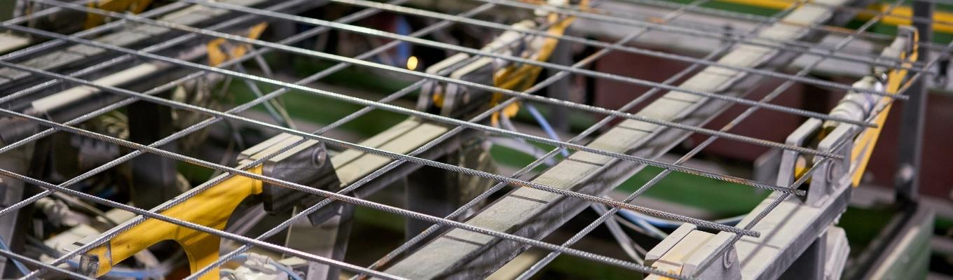 Vista próxima de vergalhões de aço em padrão de grade em um canteiro de obras, com espaçadores amarelos.