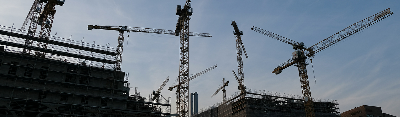 Guindastes e estruturas metálicas em canteiro de obras da construção civil.