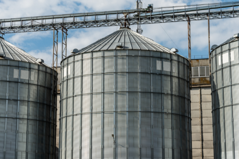 Silos metálicos de armazenamento de grãos em área rural com estrutura industrial.