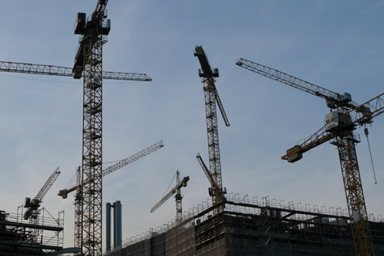 Guindastes e estruturas metálicas em canteiro de obras da construção civil.