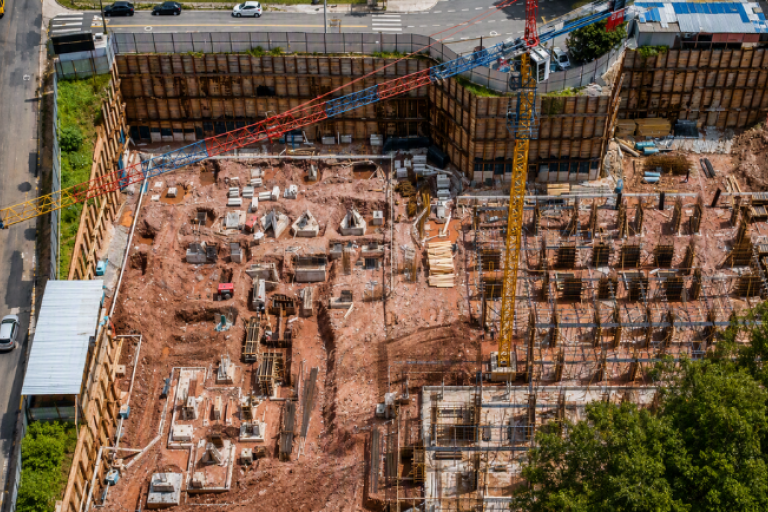 Obra com estacas metálicas e guindaste em fase de fundação.