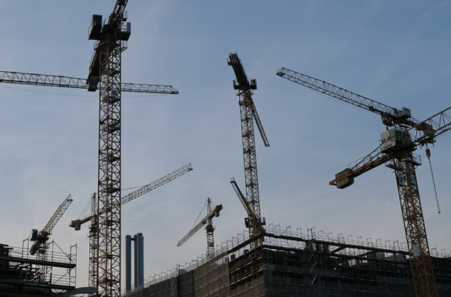 Guindastes e estruturas metálicas em canteiro de obras da construção civil.