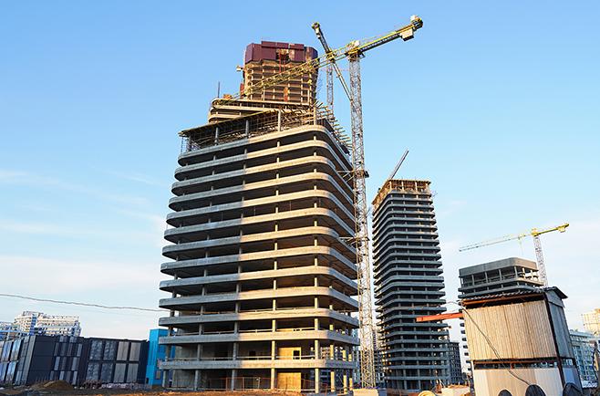 Edifícios em construção com guindastes em canteiro de obras, representando projetos da construção civil e infraestrutura.