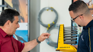 Duas pessoas interagem enquanto uma delas segura um mostruário amarelo com vergalhões de aço Gerdau em um ambiente de demonstração de produtos.