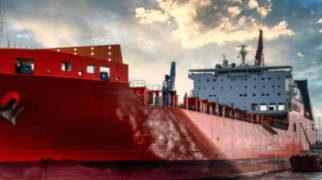 Navio de carga vermelho em estaleiro com guindastes e estrutura industrial ao fundo