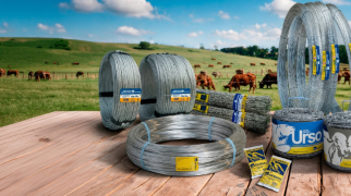 Produtos Gerdau de arame e cercamento rural dispostos em mesa de madeira, com pastagem e rebanho bovino ao fundo.