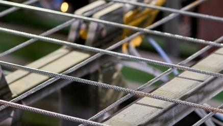 Vista próxima de vergalhões de aço em padrão de grade em um canteiro de obras, com espaçadores amarelos.